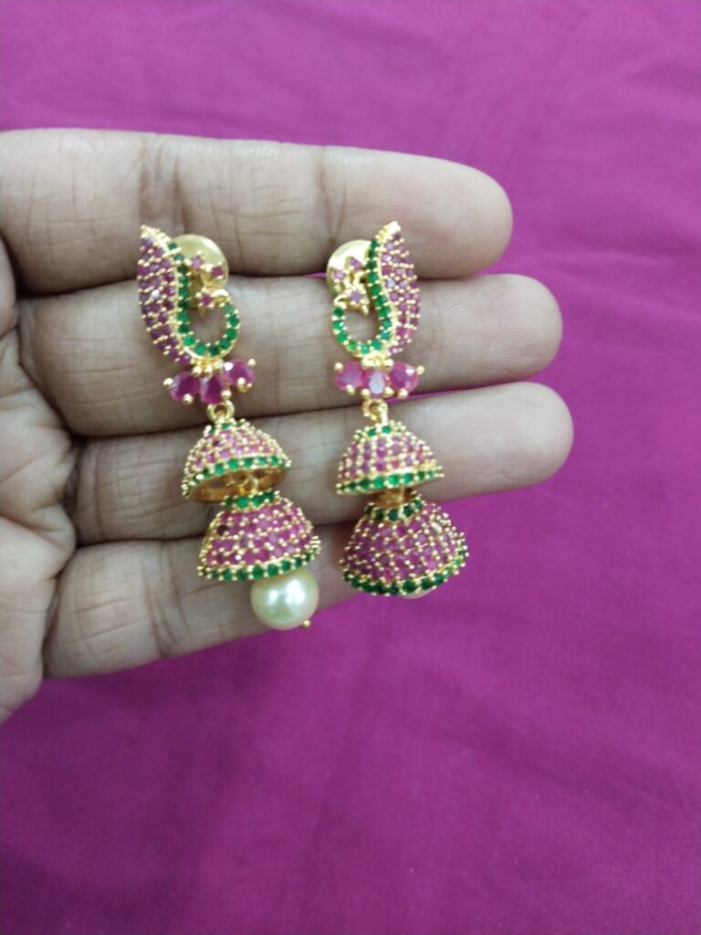 Gold double jhumka earrings with green stones and pearl drop.