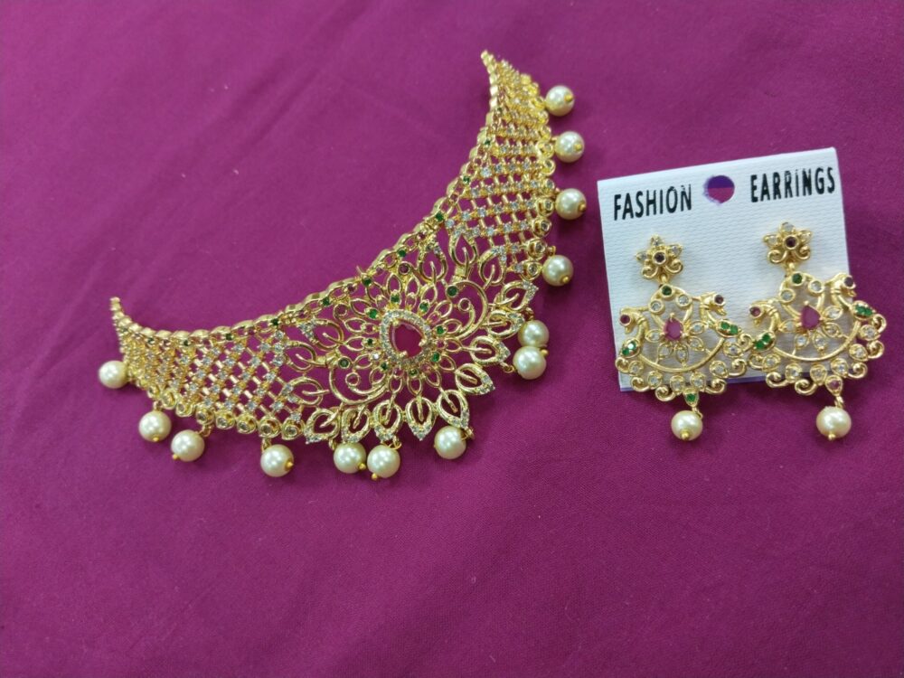 Gold mesh choker necklace with red center stone and pearl drops, paired with matching earrings on a pink background