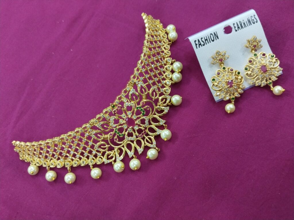 Gold filigree choker with pearl drops and matching earrings on a pink fabric background