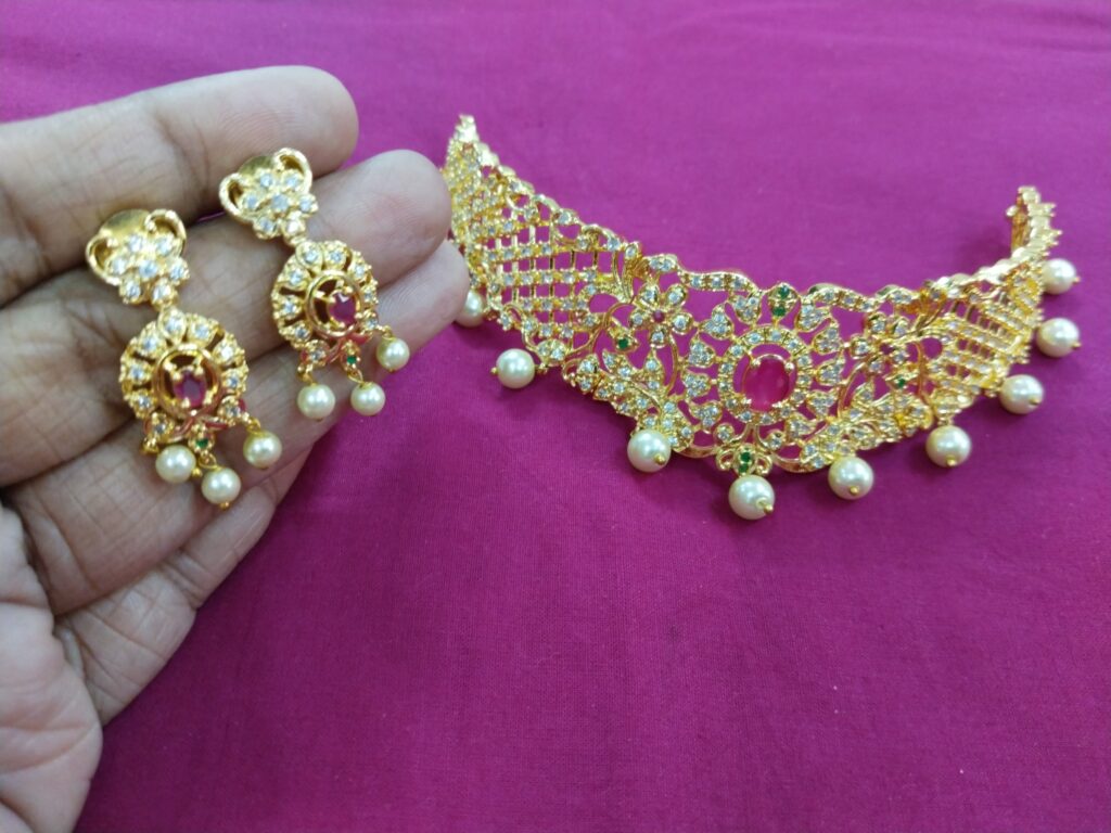 Gold choker with ruby center and pearl drops, paired with matching earrings, displayed on a pink cloth background