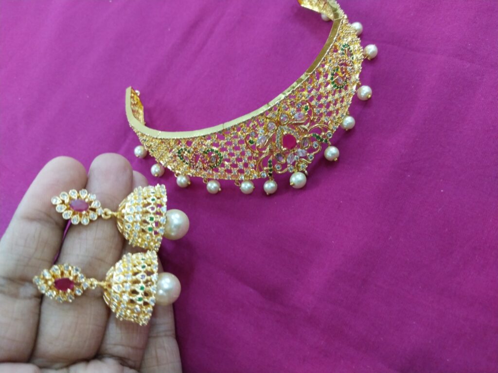 Gold mesh choker necklace with white pearl drops and matching jhumka earrings displayed on a pink background