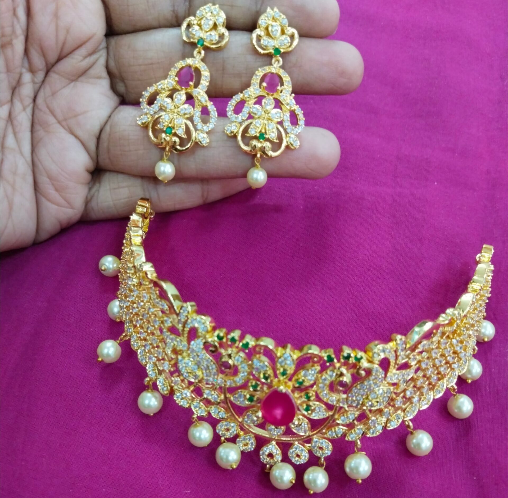 Gold plated choker necklace with ruby pink stones and pearl drops, with matching earrings, displayed on a pink background