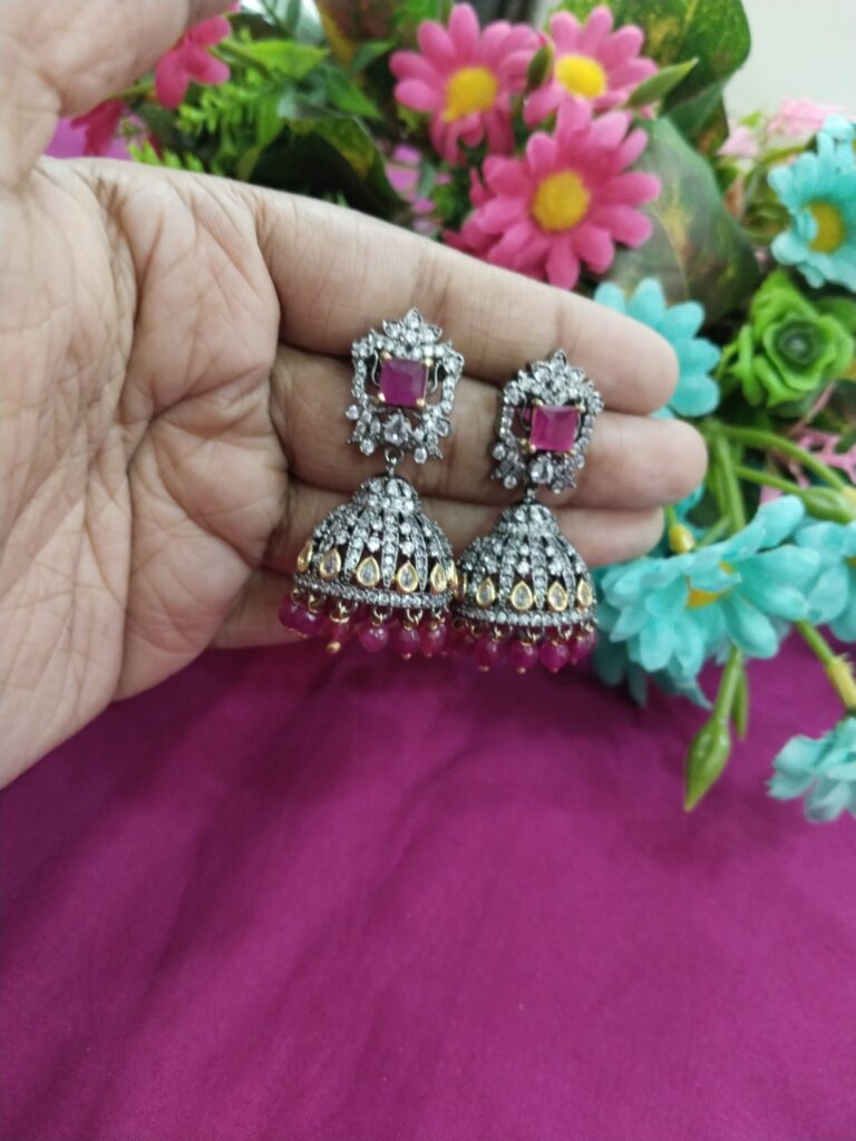 Antique silver finish jhumka earrings with ruby red stones and maroon bead drops.