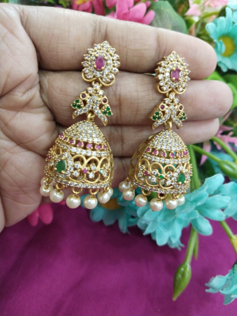 Gold-plated jhumka earrings with pink and green stones, white CZ embellishments, and pearl drops.