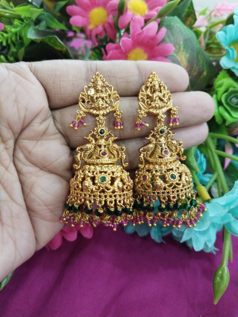 Gold-plated Lakshmi temple jhumka earrings with intricate carvings, red and green stones, and hanging magenta-green beads.
