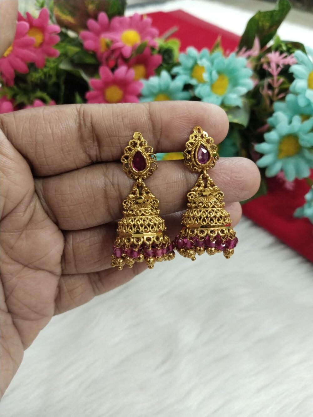 Hand holding gold plated jhumka with stones and golden danglers, traditional Indian earring