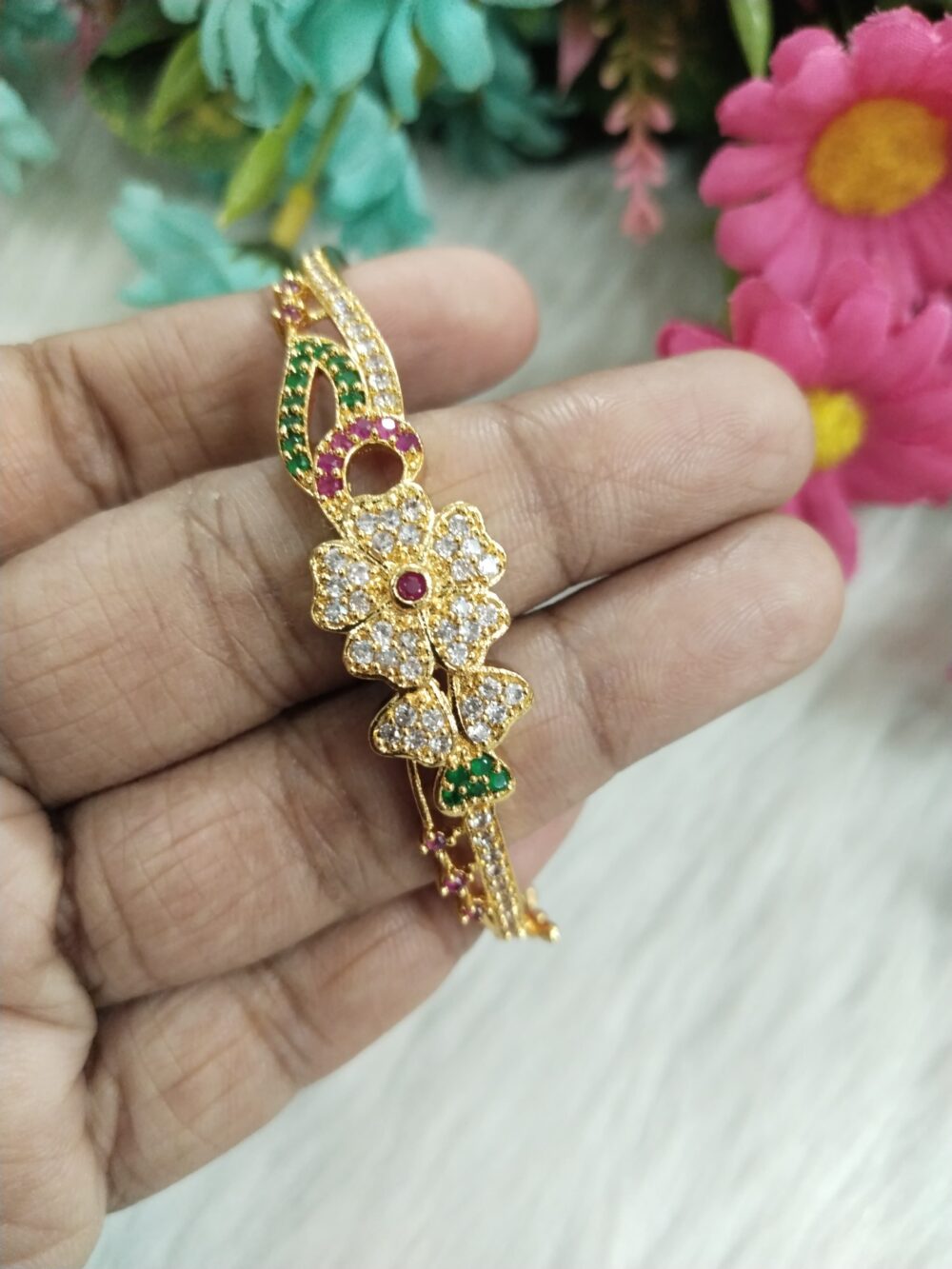 Gold-plated bangle with two flower motifs, ruby and emerald accents, and CZ stones held in hand