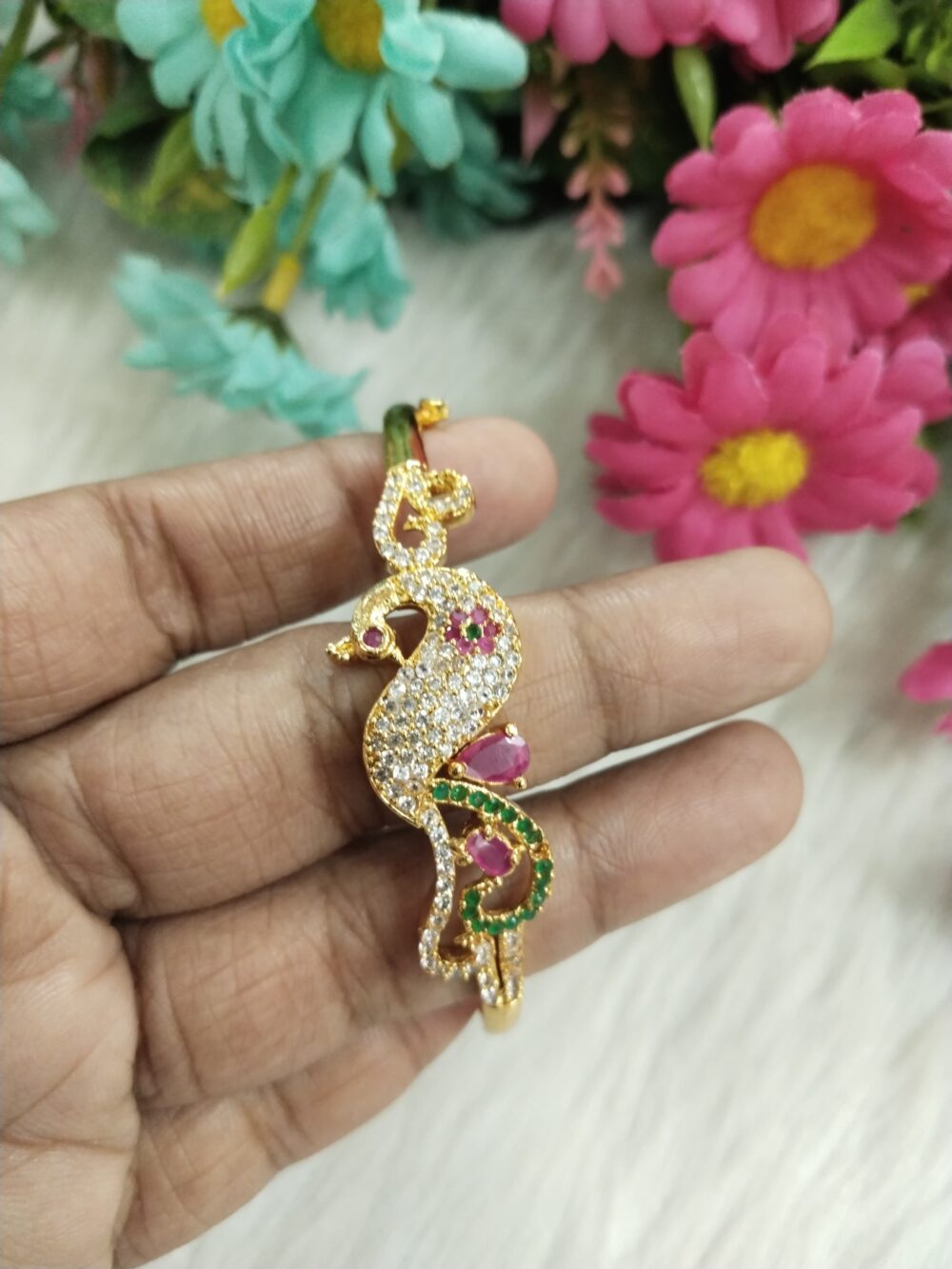 Gold-plated peacock-style bangle with ruby and emerald stones and CZ crystals held in hand