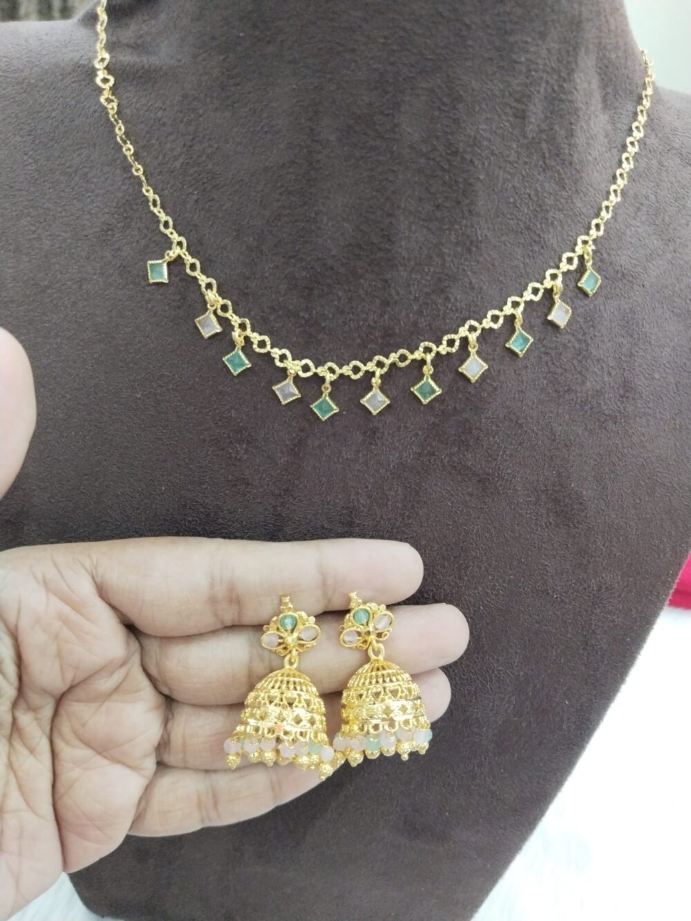 Gold-plated Indian necklace with square green and white stone drops and matching jhumka earrings held in hand