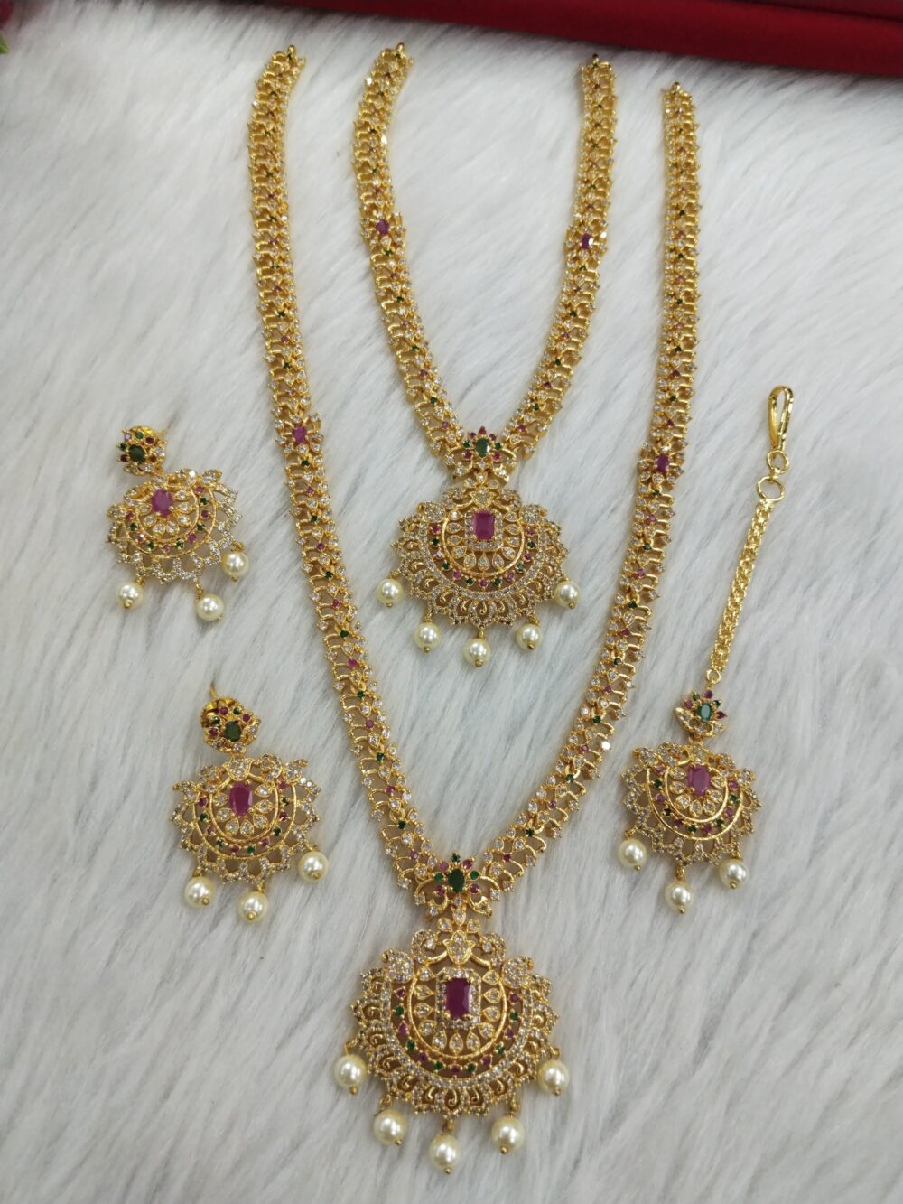 Traditional gold-plated Indian bridal jewelry set with ruby rectangular stones, green accents, and pearl hangings on a white background